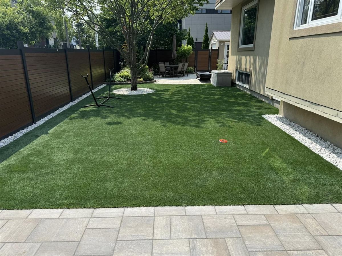 A back yard bounded by a dark horizontal-slat privacy fence, with turf and a stone border