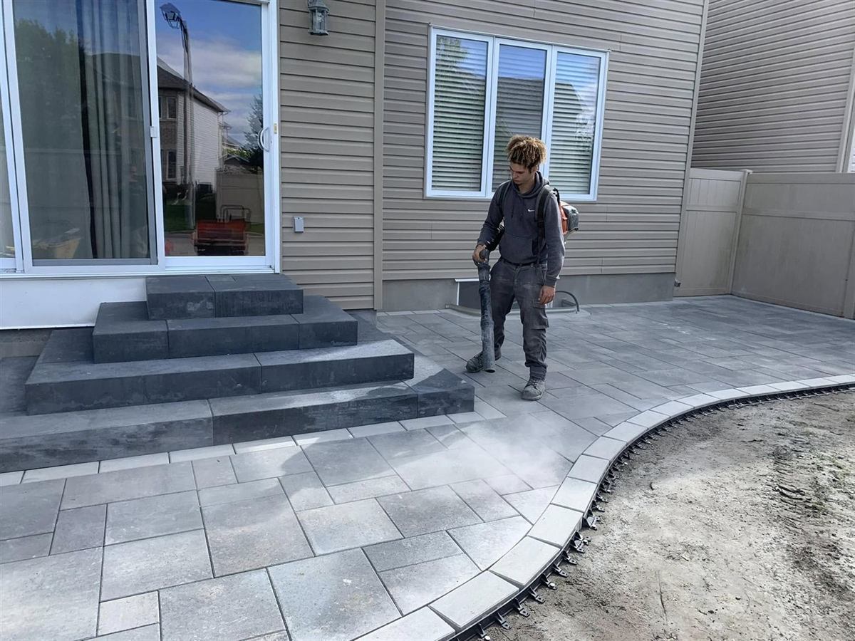 A crew member blowing down a freshly finished paver patio