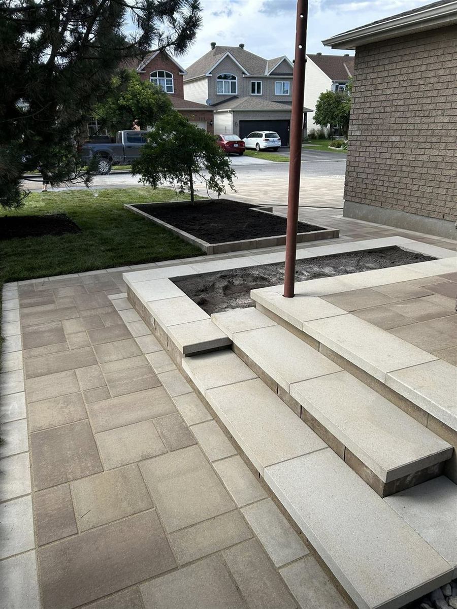 A new front entrance: slab steps up to an interlock landing beside a capped raised bed, with fresh sod and the paver driveway beyond