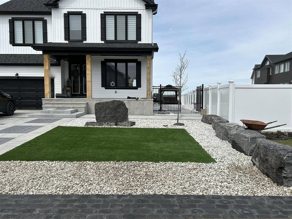 A front yard finished with artificial turf, white decorative stone and placed granite boulders