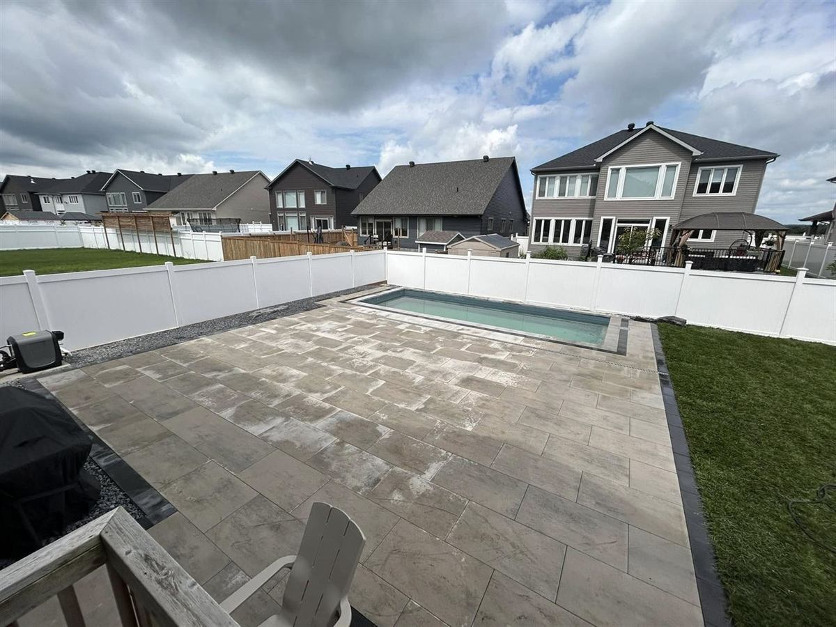 A rectangular pool set into a full paver deck with dark coping and a privacy fence beyond