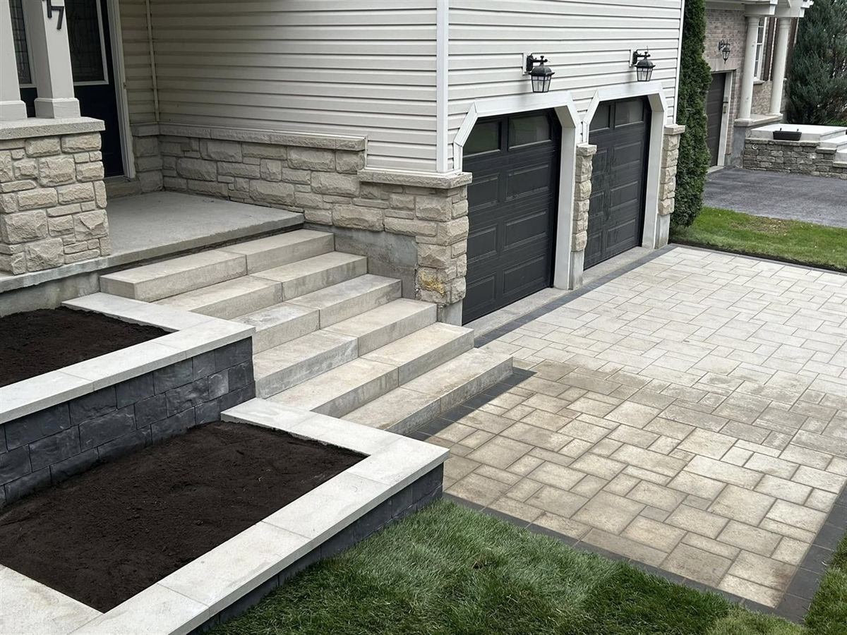 A front entrance with slab steps, a capped raised planter, fresh sod and an interlock driveway